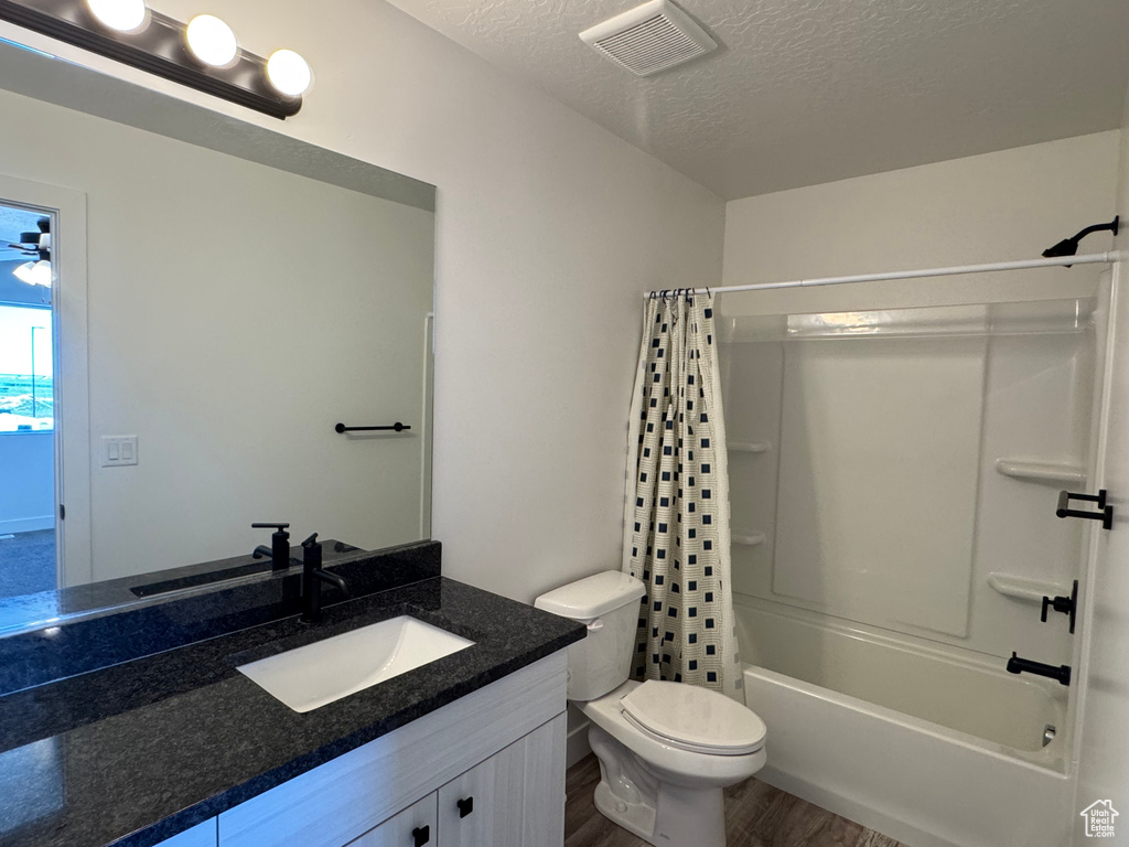 Full bath with a textured ceiling, toilet, vanity, wood finished floors, and shower / bath combo with shower curtain