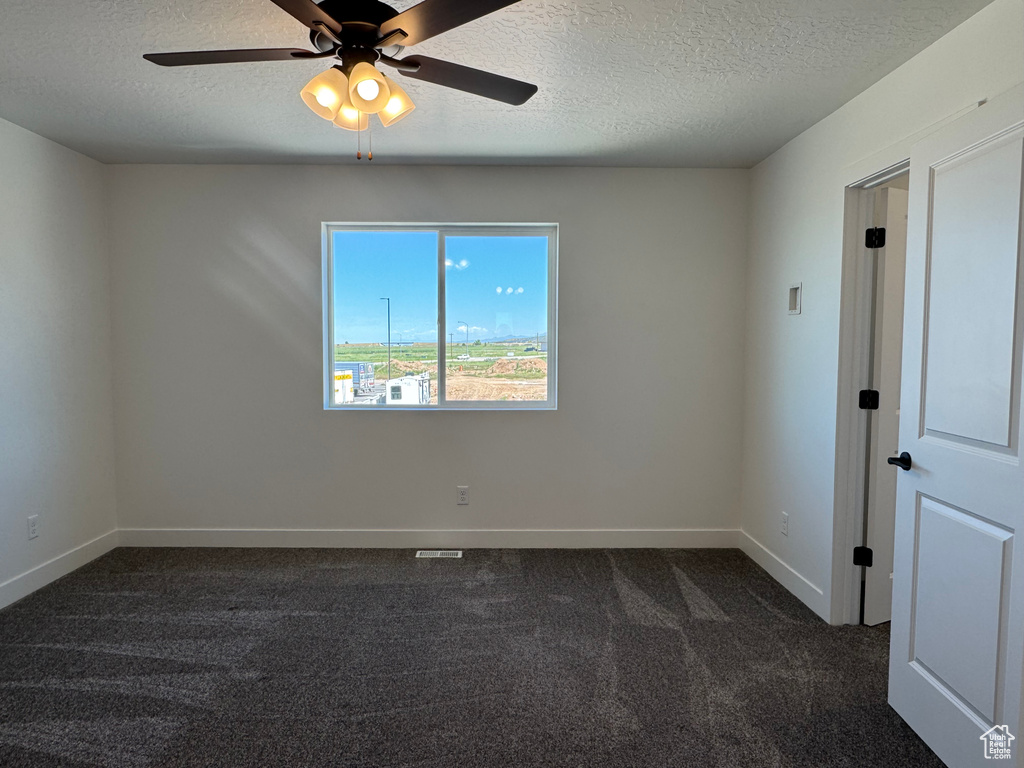 Empty room with a textured ceiling, dark carpet, baseboards, and a ceiling fan