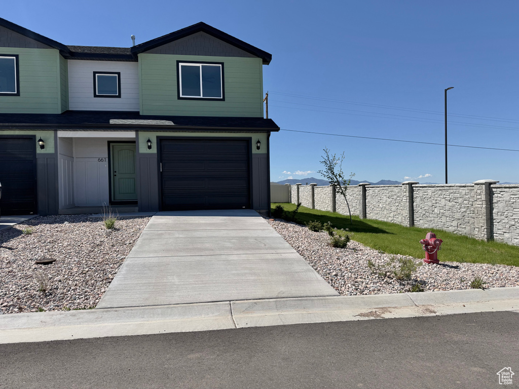 View of front facade featuring fence, concrete driveway, and a garage