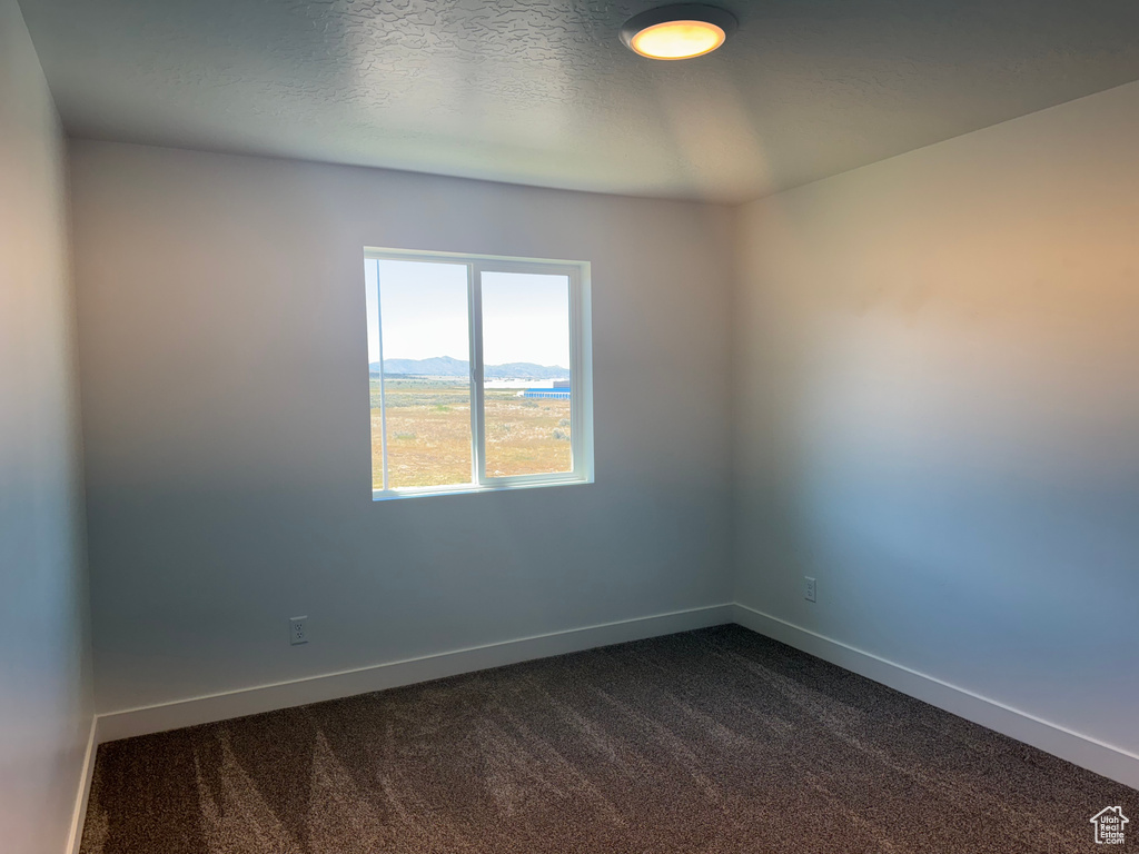 Unfurnished room featuring dark carpet and baseboards