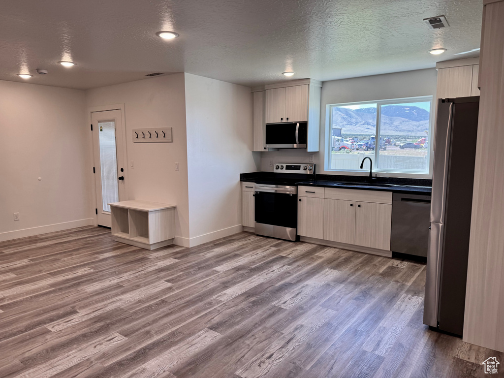 Kitchen featuring appliances with stainless steel finishes, a sink, light wood-style flooring, dark countertops, and baseboards
