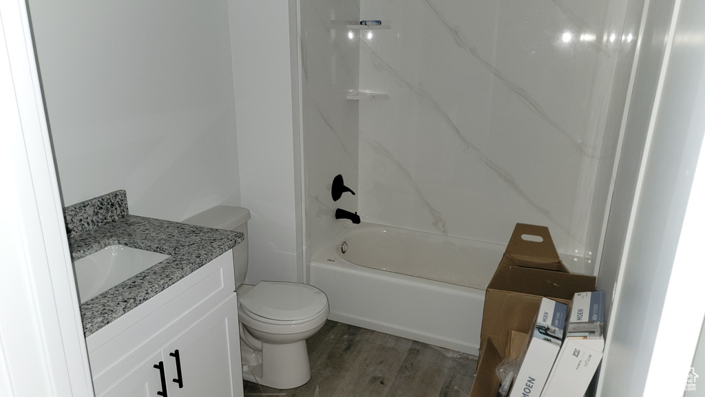 Bathroom featuring wood finished floors, vanity, toilet, and washtub / shower combination