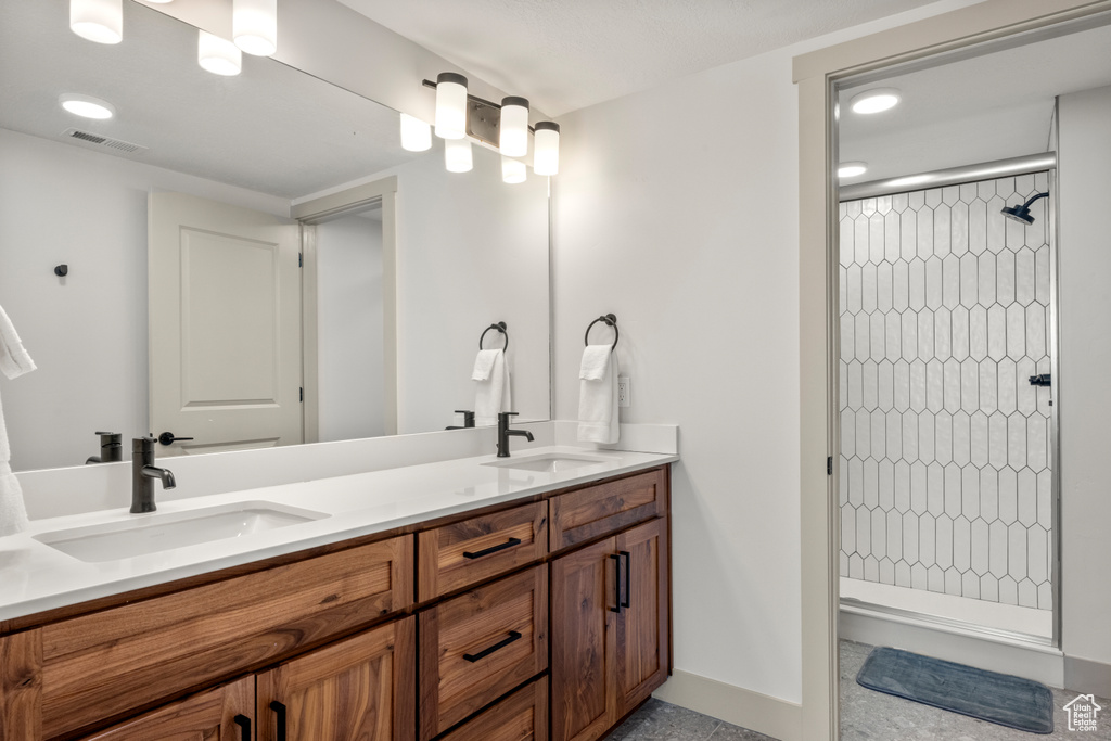Bathroom with tiled shower, double vanity, baseboards, and recessed lighting
