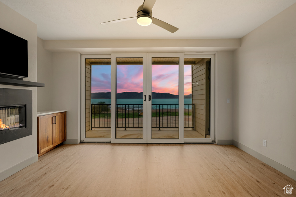 Unfurnished living room featuring light wood-style floors, a glass covered fireplace, a ceiling fan, and baseboards