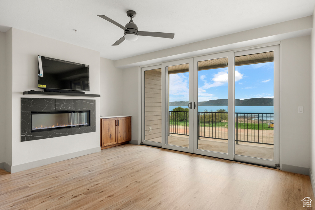 Unfurnished living room with light wood-style floors, a premium fireplace, a ceiling fan, and baseboards