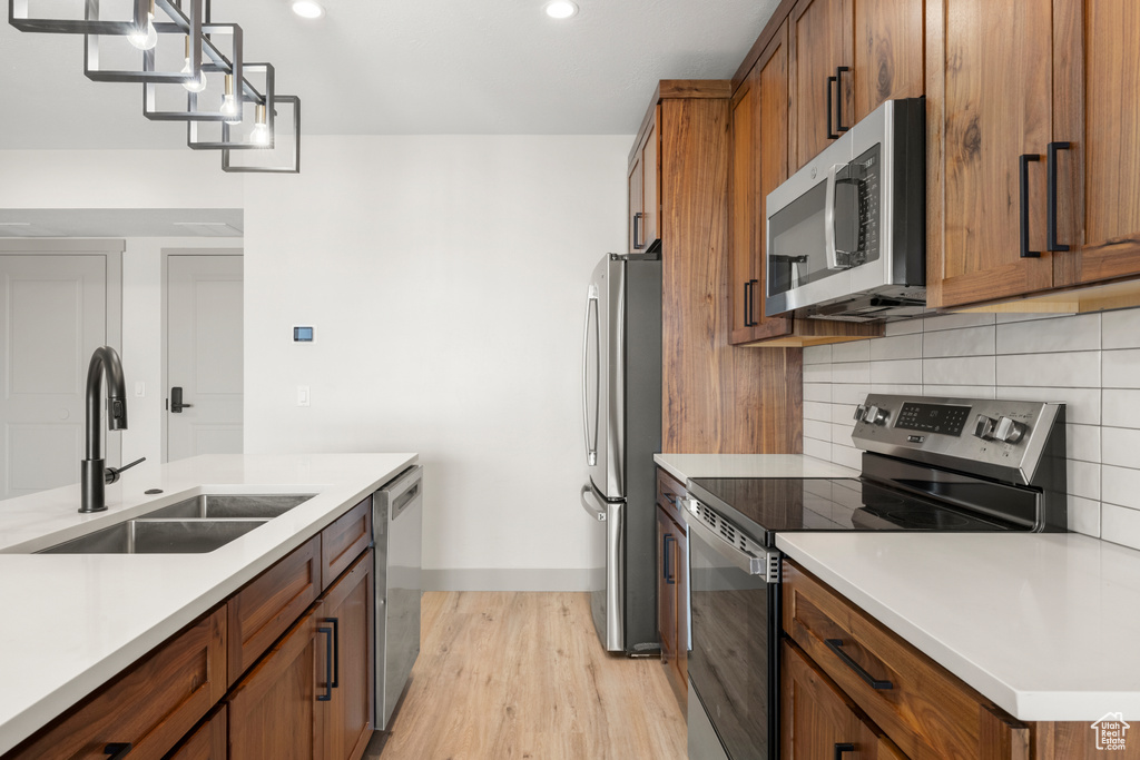 Kitchen featuring stainless steel appliances, a sink, light wood-type flooring, brown cabinetry, and recessed lighting