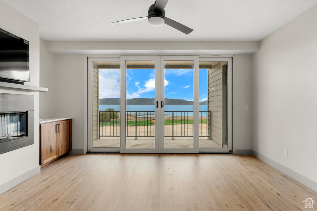 Unfurnished living room featuring light wood-style flooring, a ceiling fan, a glass covered fireplace, and baseboards
