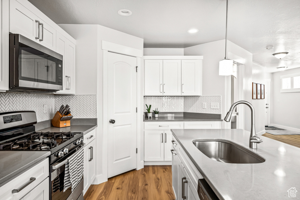 Kitchen with stainless steel appliances, a sink, light wood finished floors, white cabinetry, and recessed lighting