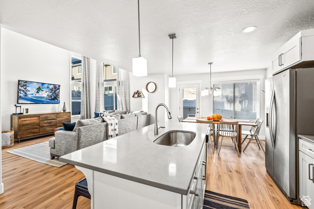 Kitchen featuring a sink, stainless steel refrigerator with ice dispenser, an island with sink, light wood-style floors, and white cabinetry
