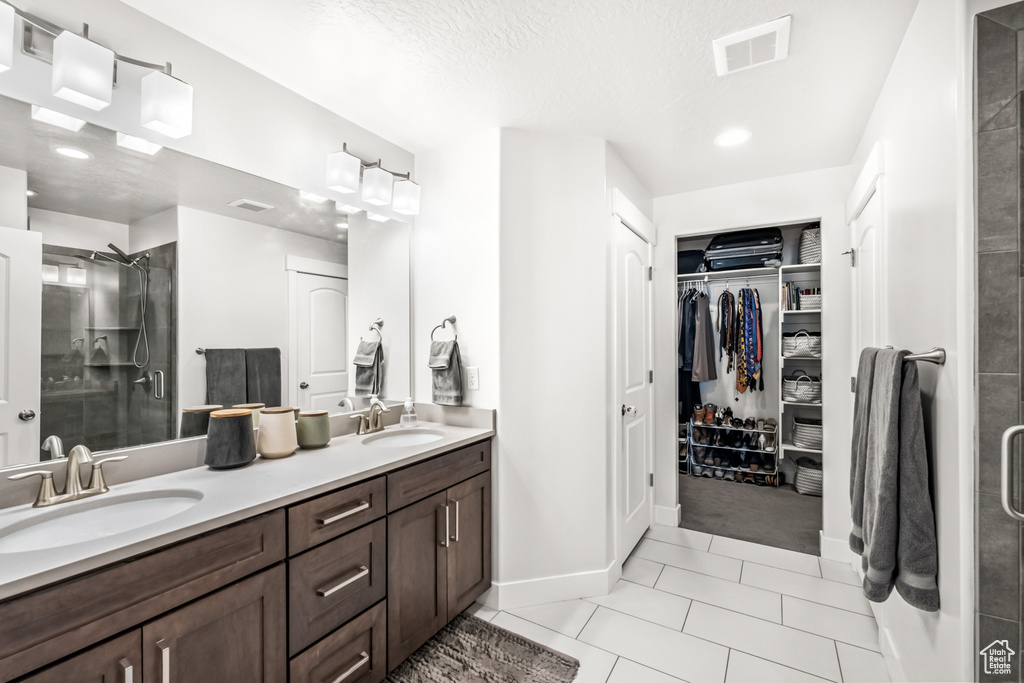 Bathroom featuring a stall shower, double vanity, a walk in closet, tile patterned floors, and baseboards