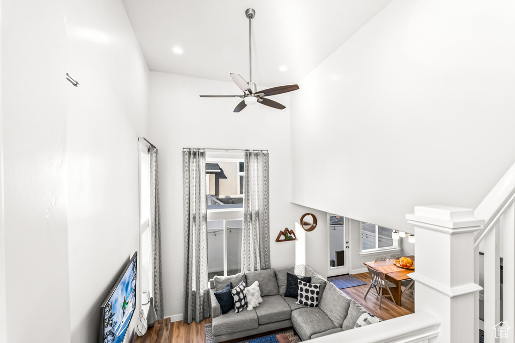 Living area with wood finished floors, a towering ceiling, a ceiling fan, healthy amount of natural light, and recessed lighting