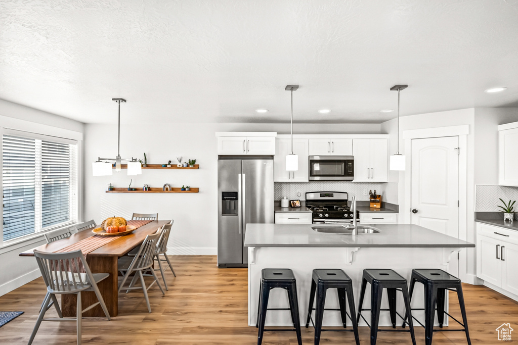 Kitchen with appliances with stainless steel finishes, dark countertops, backsplash, a kitchen breakfast bar, and light wood finished floors