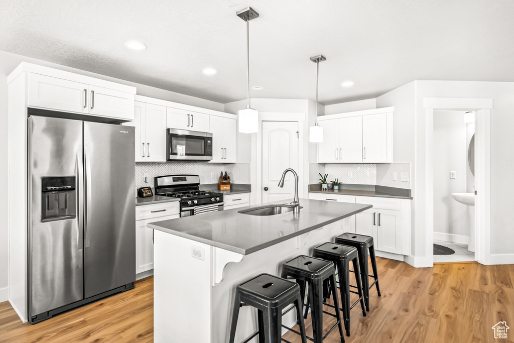 Kitchen with appliances with stainless steel finishes, a sink, dark countertops, light wood-style flooring, and a breakfast bar