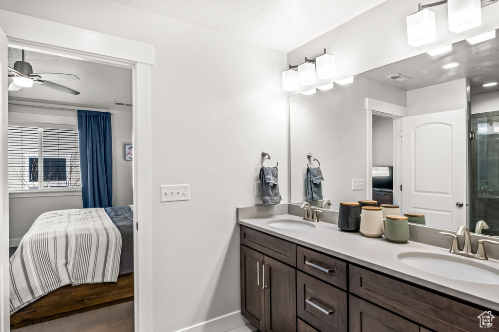 Bathroom featuring ensuite bath, baseboards, double vanity, a shower with shower door, and ceiling fan