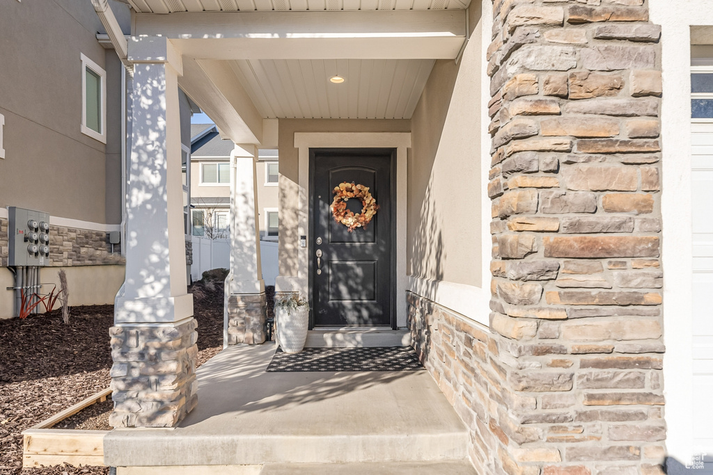 Doorway to property featuring stone siding, stucco siding, and covered porch