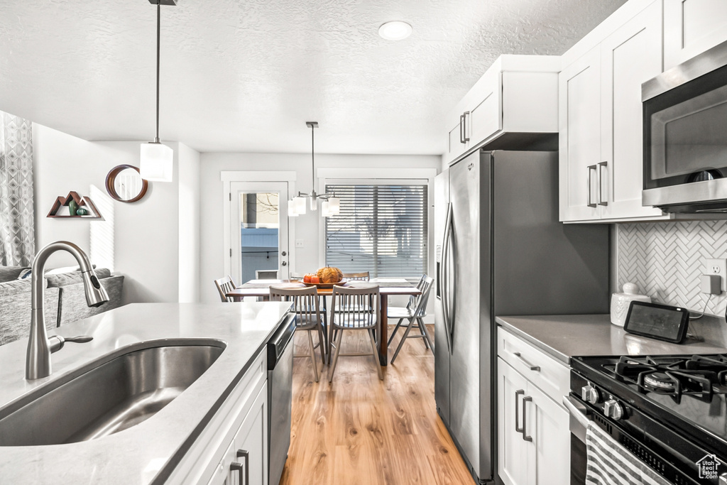 Kitchen featuring stainless steel appliances, a sink, light wood-style flooring, decorative backsplash, and white cabinets