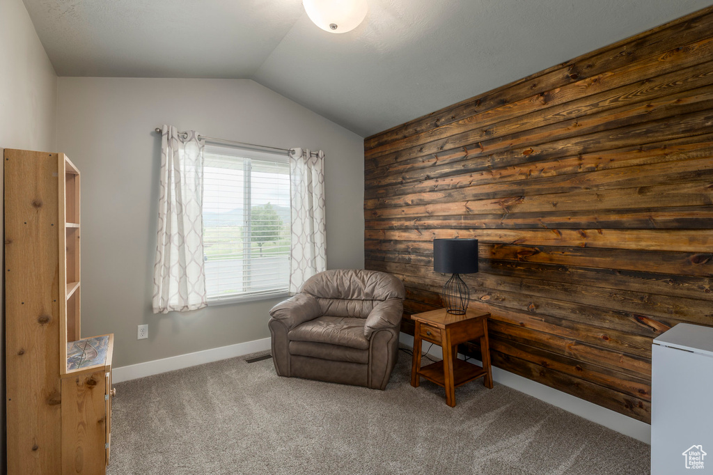Living area with dark colored carpet, vaulted ceiling, and wooden walls