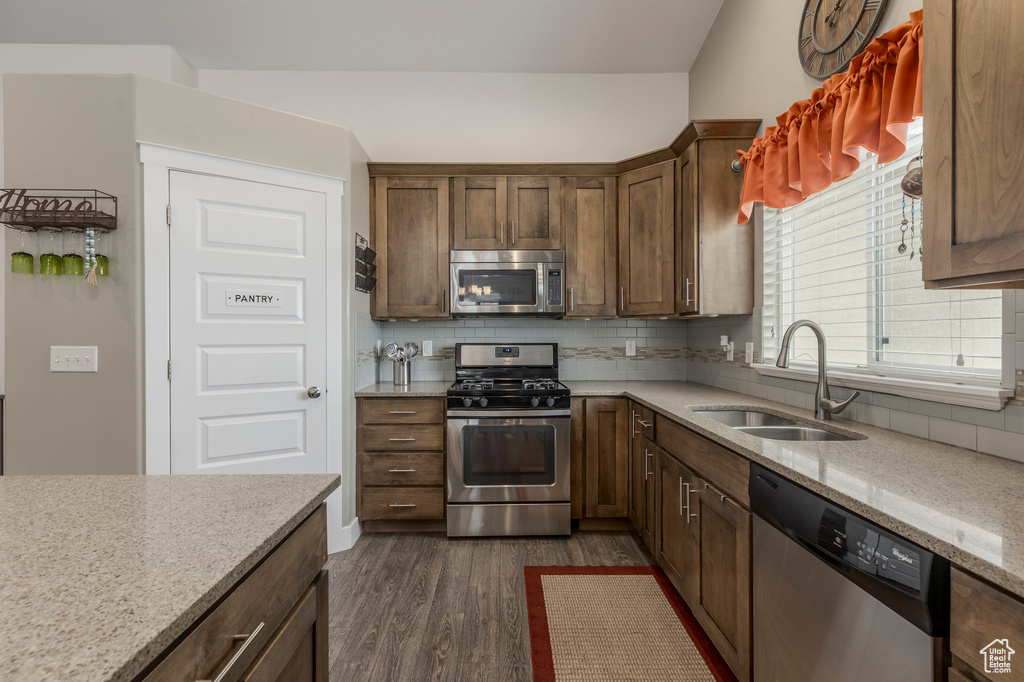 Kitchen featuring appliances with stainless steel finishes, a sink, dark wood-style floors, tasteful backsplash, and light stone counters