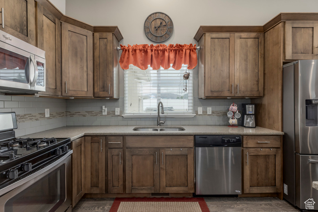 Kitchen with stainless steel appliances, a sink, decorative backsplash, and dark wood-type flooring