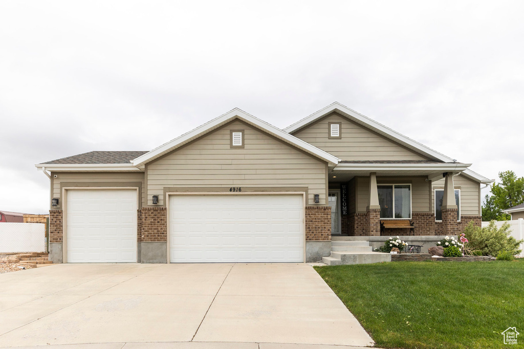 View of front of home with a garage, brick siding, a front yard, concrete driveway, and covered porch