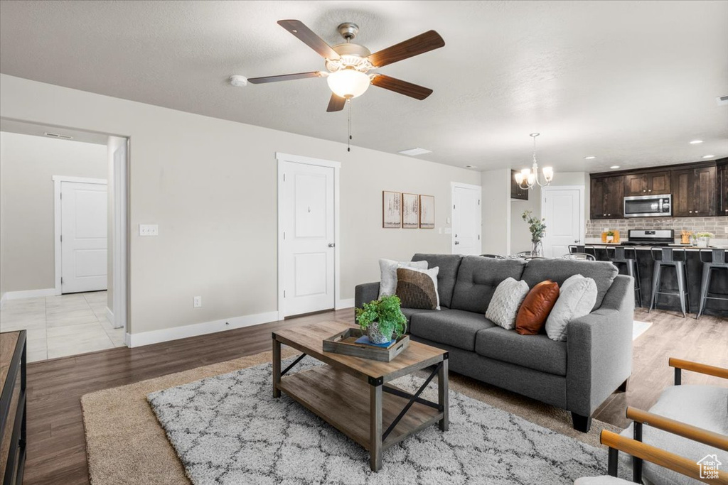 Living room featuring a chandelier, ceiling fan, baseboards, light wood finished floors, and recessed lighting