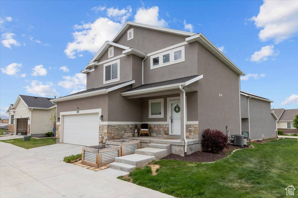 View of front of property featuring concrete driveway, an attached garage, stucco siding, central AC, and a front yard