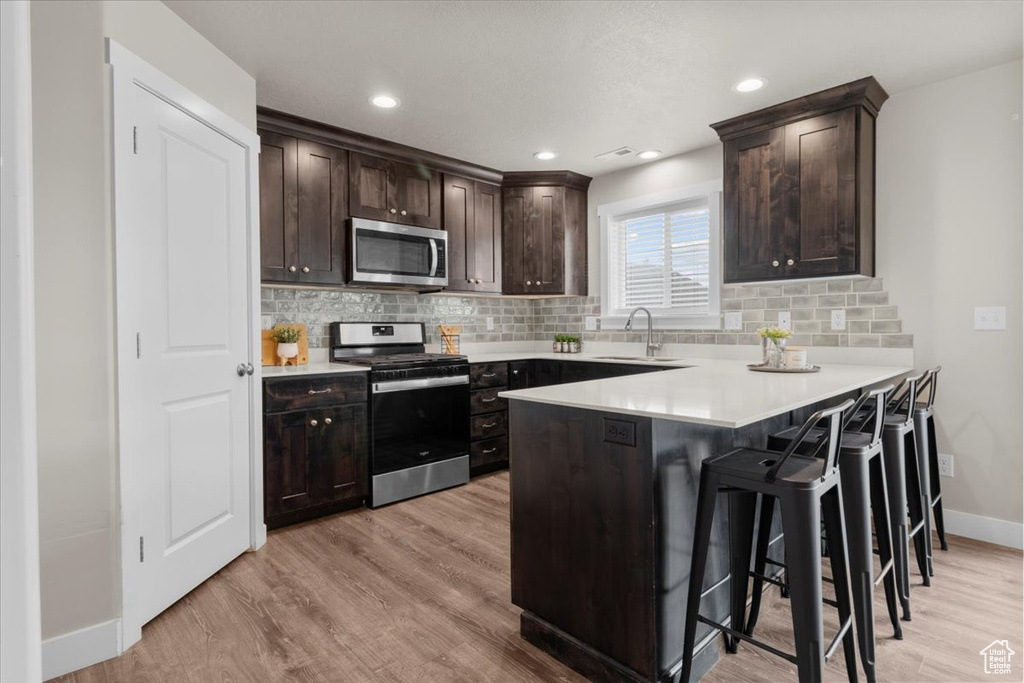 Kitchen featuring stainless steel appliances, a sink, baseboards, light wood-style floors, and recessed lighting