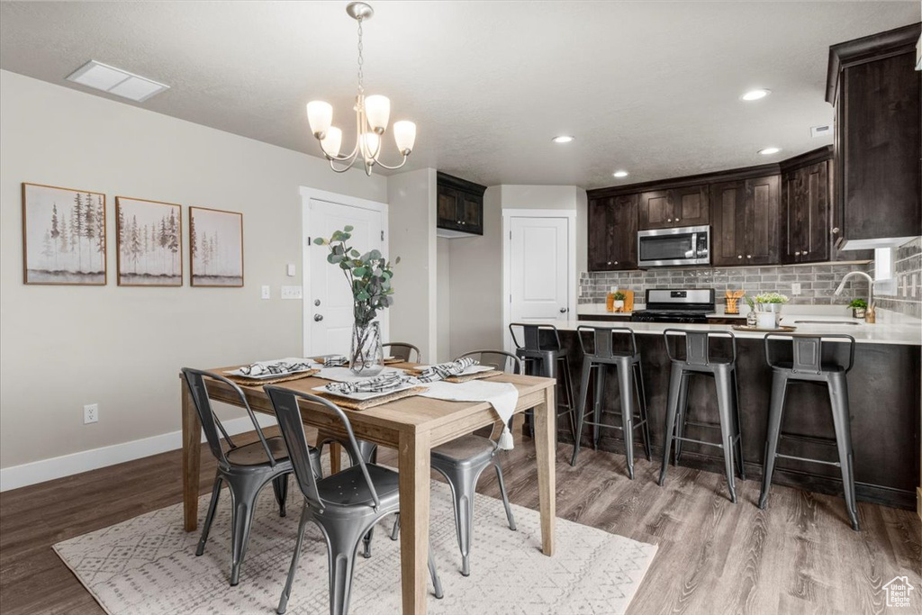 Dining room with light wood-type flooring, baseboards, a chandelier, and recessed lighting