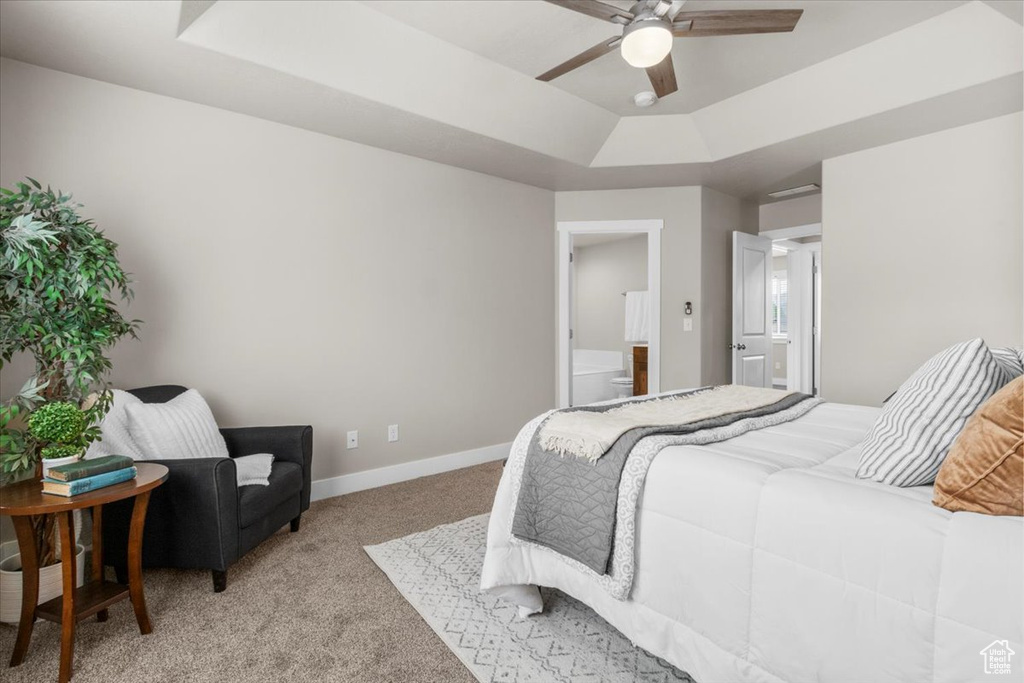 Bedroom with a raised ceiling, light colored carpet, baseboards, connected bathroom, and a ceiling fan