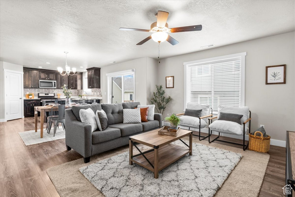 Living area with a chandelier, a ceiling fan, light wood-type flooring, baseboards, and a textured ceiling
