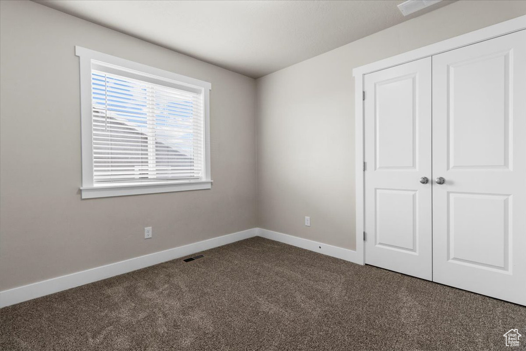 Unfurnished bedroom featuring dark colored carpet, baseboards, and a closet
