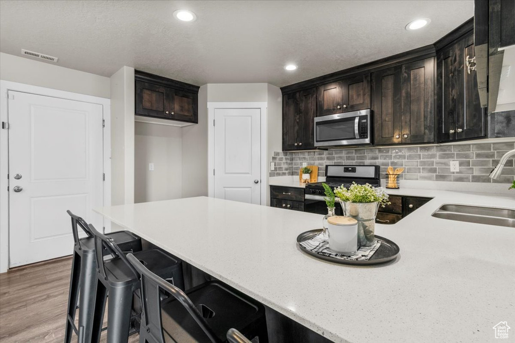 Kitchen featuring stainless steel appliances, a sink, backsplash, recessed lighting, and wood finished floors