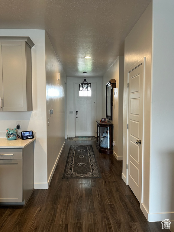 Foyer with baseboards, dark wood-type flooring, a textured ceiling, and a chandelier