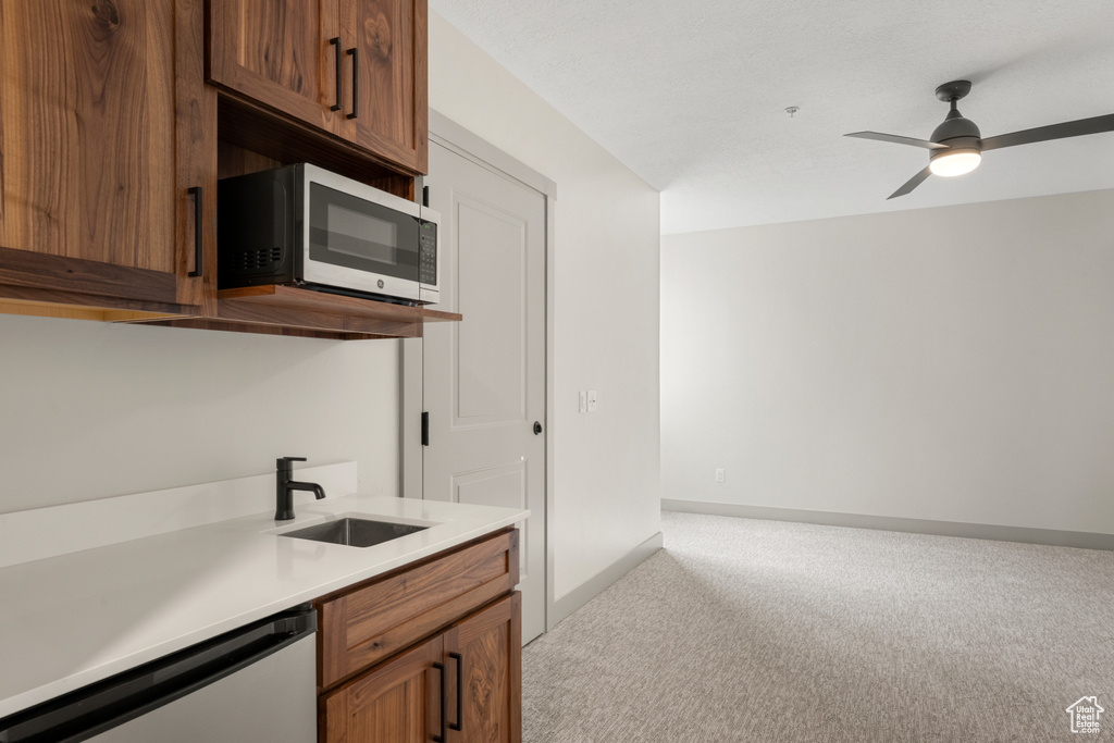 Kitchen featuring appliances with stainless steel finishes, light colored carpet, a sink, light countertops, and ceiling fan