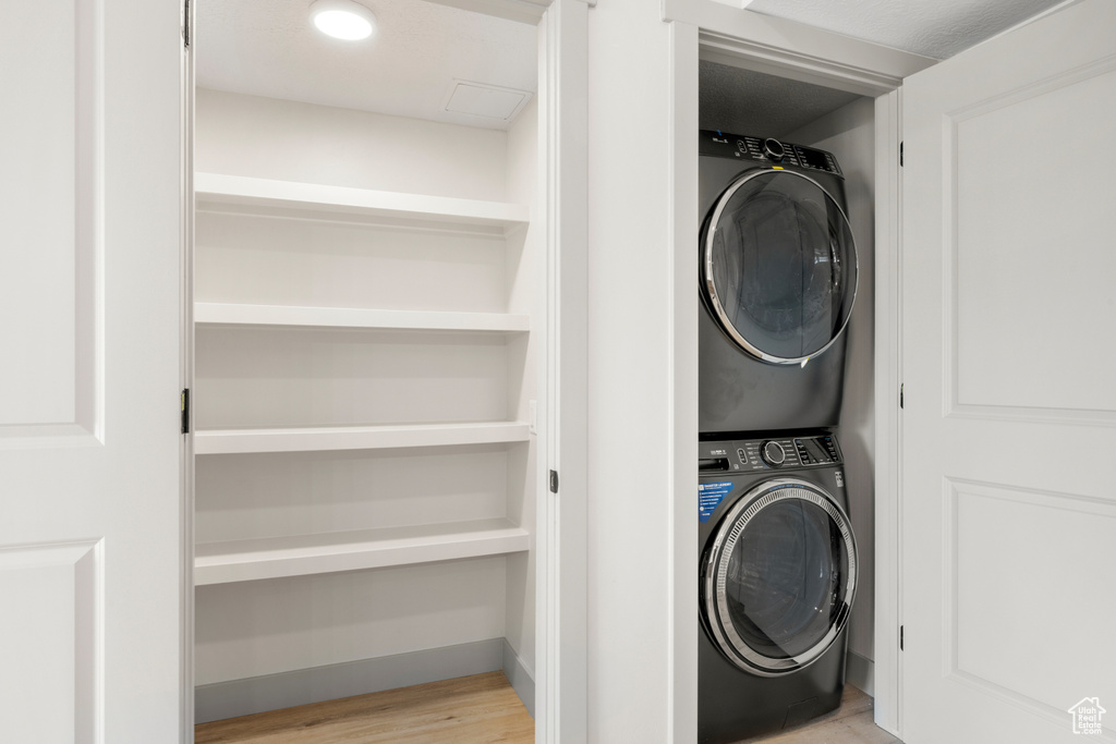 Laundry room with stacked washing machine and dryer and wood finished floors