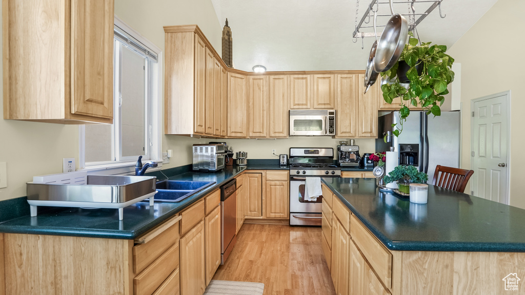 Kitchen featuring stainless steel appliances, light brown cabinetry, dark countertops, light wood-type flooring, and a kitchen island