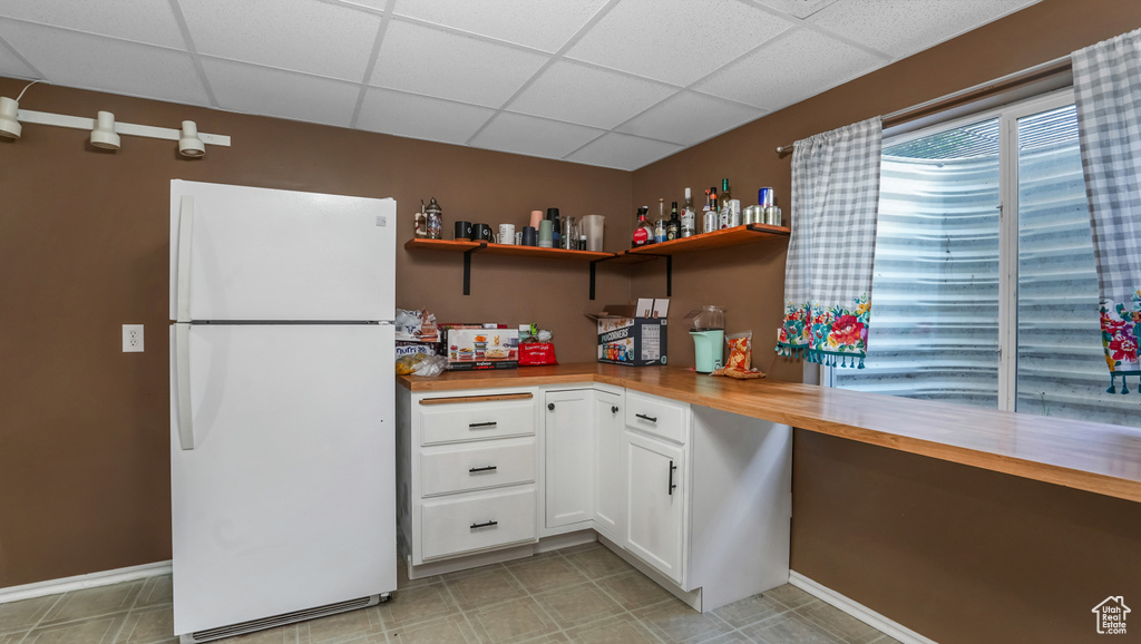 Kitchen with freestanding refrigerator, a paneled ceiling, white cabinetry, open shelves, and baseboards