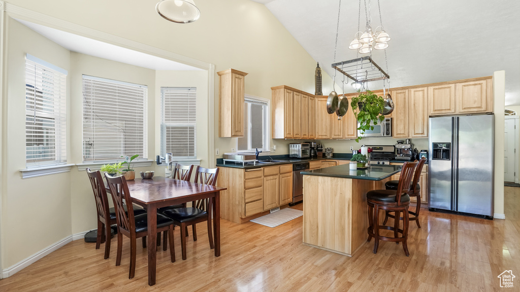 Kitchen featuring appliances with stainless steel finishes, high vaulted ceiling, light brown cabinets, light wood-style floors, and a kitchen island
