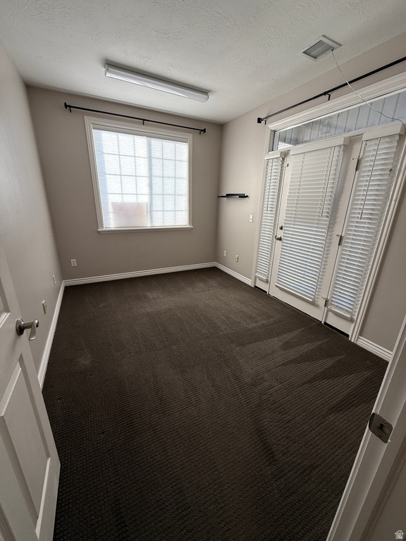 Empty room featuring a textured ceiling and dark colored carpet