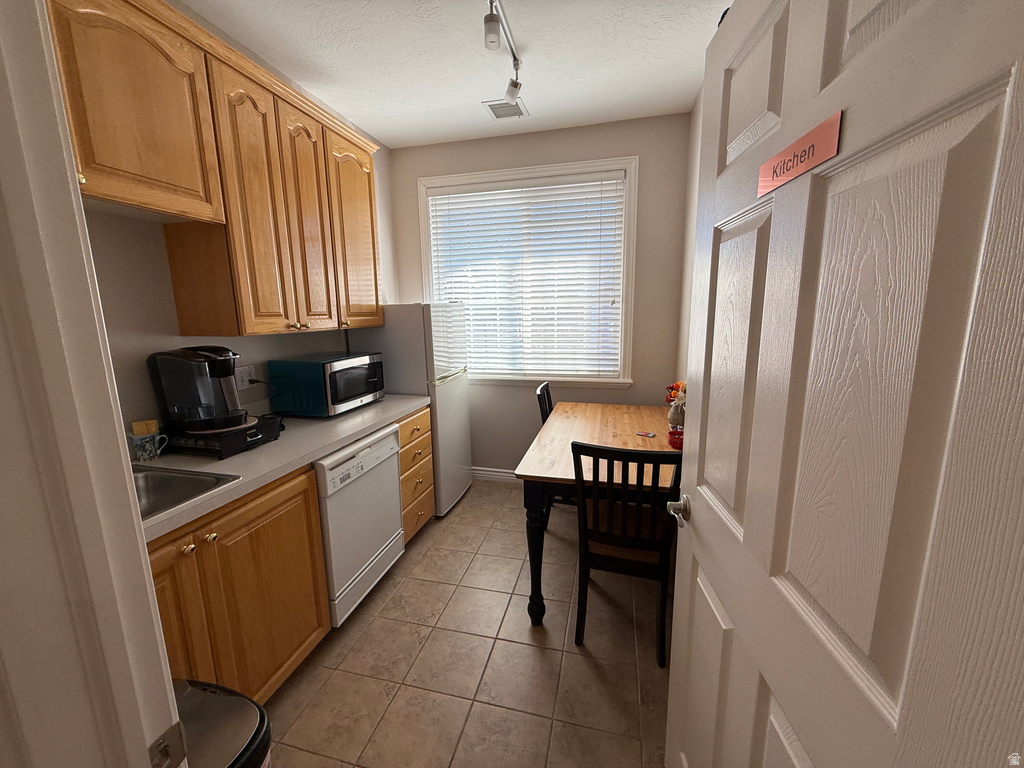 Kitchen with light countertops, light tile patterned floors, white appliances, a textured ceiling, and rail lighting