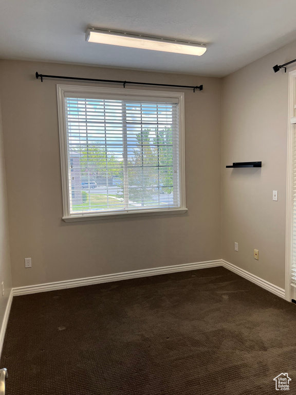 Empty room with plenty of natural light, dark carpet, and baseboards