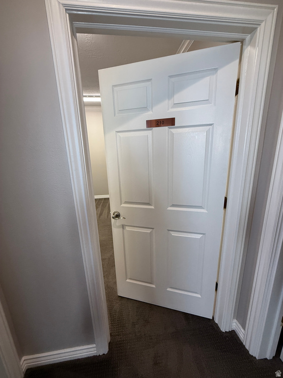 Hallway with baseboards and dark carpet
