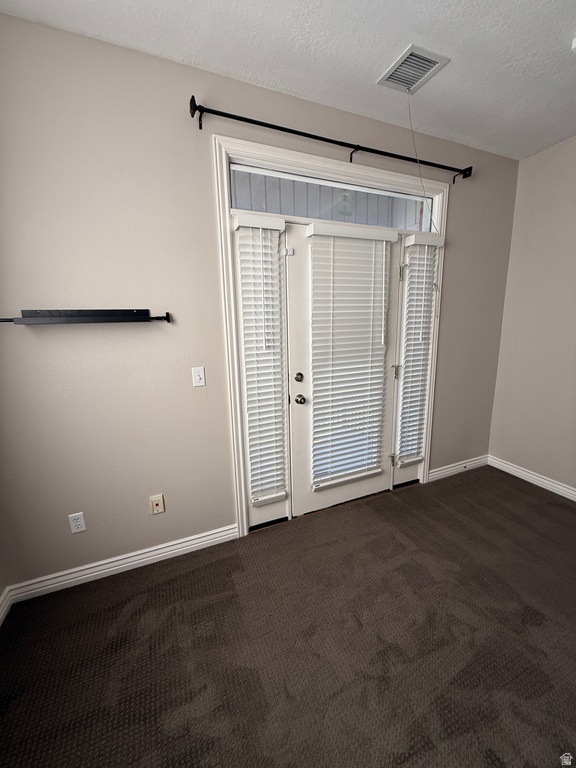 Empty room featuring dark colored carpet and a textured ceiling