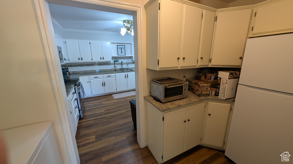 Kitchen featuring freestanding refrigerator, dark wood-style flooring, crown molding, a ceiling fan, and white cabinetry