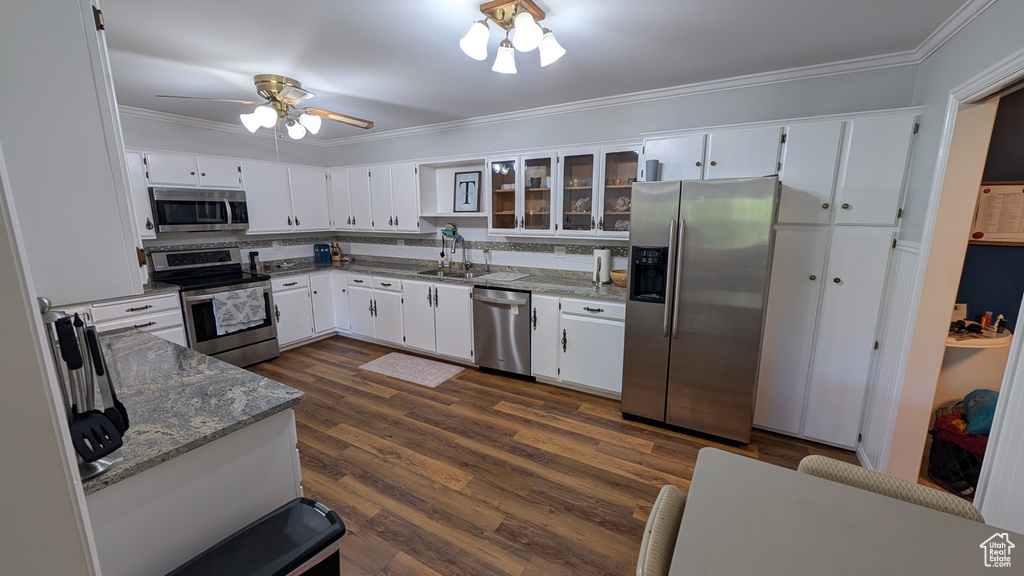 Kitchen with stainless steel appliances, ornamental molding, white cabinetry, stone countertops, and dark wood finished floors