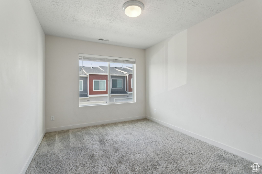 Carpeted spare room with a textured ceiling and baseboards