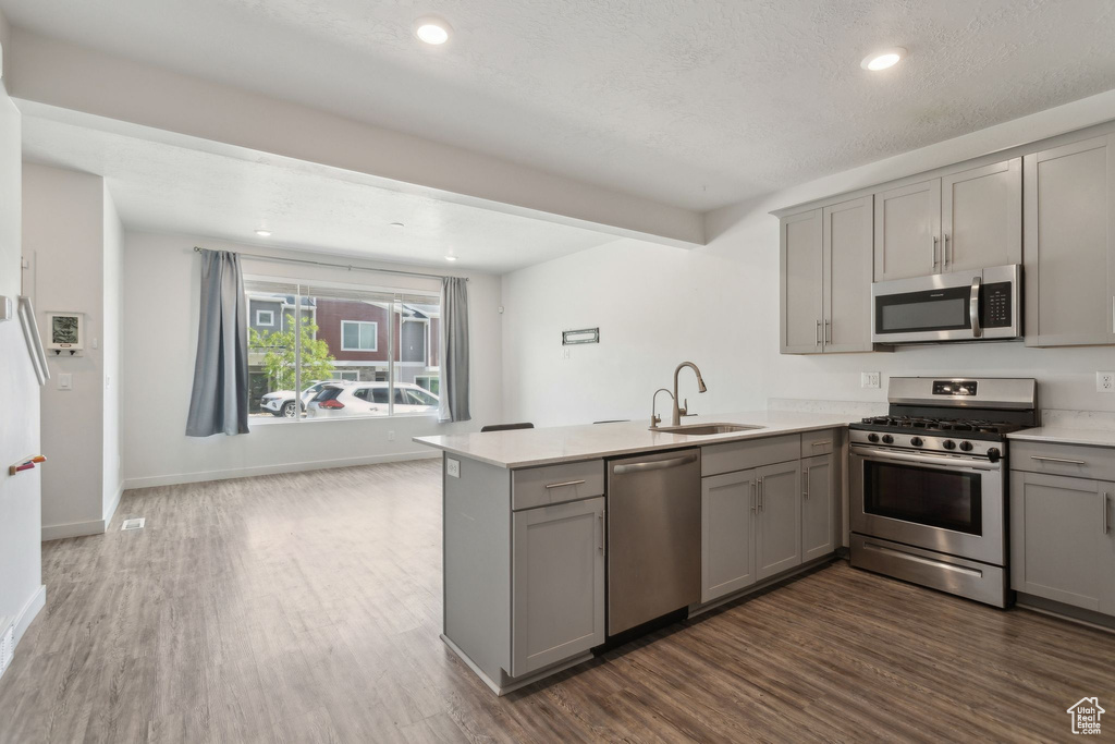 Kitchen with stainless steel appliances, gray cabinets, a peninsula, a sink, and recessed lighting
