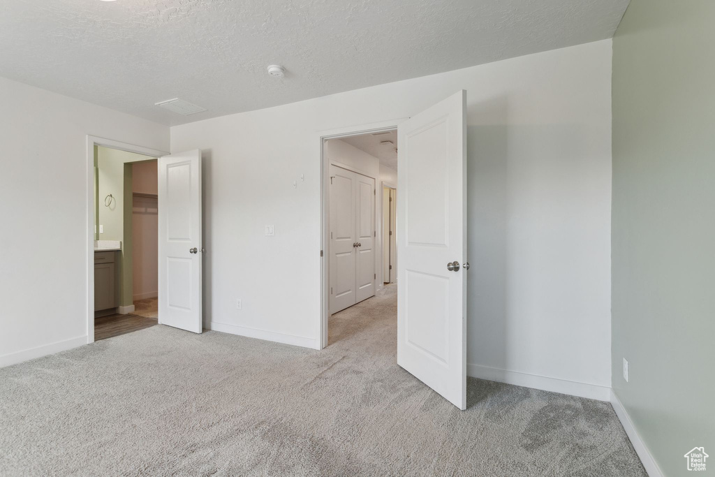Unfurnished bedroom featuring light colored carpet, baseboards, and a textured ceiling