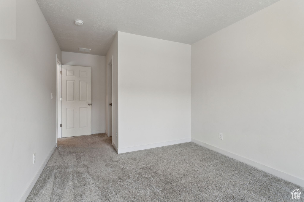 Carpeted spare room with baseboards, a textured ceiling, and a smoke detector