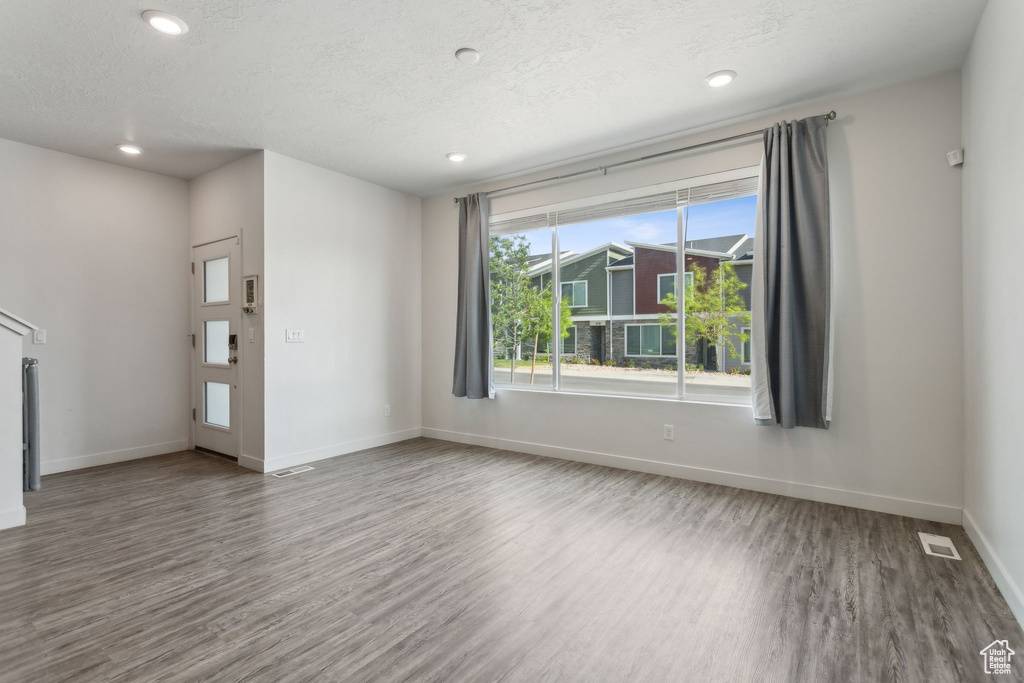 Unfurnished living room featuring wood finished floors, baseboards, recessed lighting, and a textured ceiling